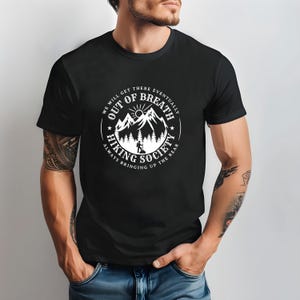 Może przedstawiać: Czarna koszulka z białym okrągłym nadrukiem przedstawiającym g&oacute;ry, słońce i turystę. Tekst brzmi "Out of Breath Hiking Society" i "We will get there eventually, always bringing up the rear."