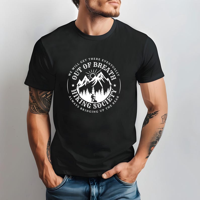 Może przedstawiać: Czarna koszulka z białym okrągłym nadrukiem przedstawiającym g&oacute;ry, słońce i turystę. Tekst brzmi "Out of Breath Hiking Society" i "We will get there eventually, always bringing up the rear."
