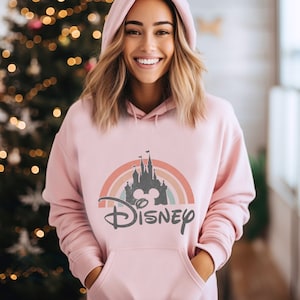 May include: Pink hoodie featuring a rainbow and a silhouette of Cinderella's castle with Mickey Mouse ears in front of it. The text "DISNEY" is below the castle.