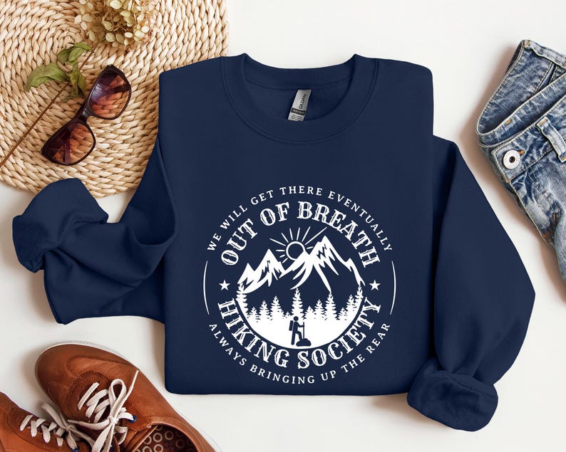 Może przedstawiać: Granatowa bluza z białym nadrukiem. Okrągła grafika zawiera tekst "We Will Get There Eventually Out of Breath Hiking Society Always Bringing Up The Rear" z motywem g&oacute;r i turysty.