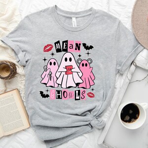Pu&ograve; includere: Maglietta grigia con una grafica rosa e bianca di tre fantasmi. Il testo "Mean Ghouls" &egrave; scritto in nero con accenti rosa.
