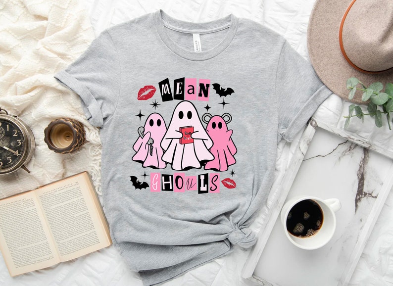 Pu&ograve; includere: Maglietta grigia con una grafica rosa e bianca di tre fantasmi. Il testo "Mean Ghouls" &egrave; scritto in nero con accenti rosa.