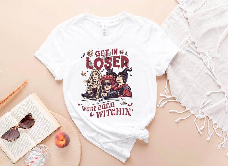 May include: White t-shirt with a graphic of three witches driving in a car. The text on the shirt reads "Get in Loser, We're Going Witchin'"