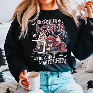 May include: Black sweatshirt with a graphic print of three witches driving in a car. The text on the shirt reads "Get in Loser, We're Going Witchin'"