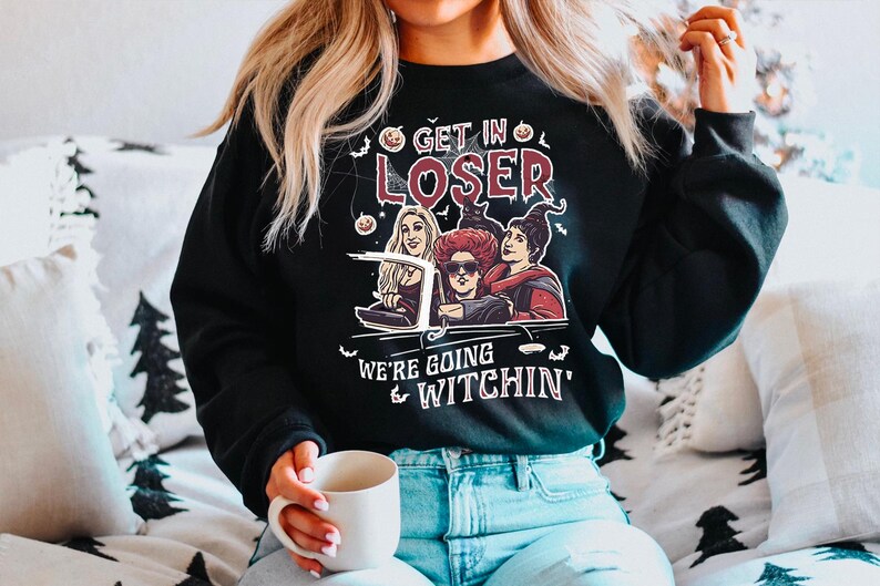 May include: Black sweatshirt with a graphic print of three witches driving in a car. The text on the shirt reads "Get in Loser, We're Going Witchin'"