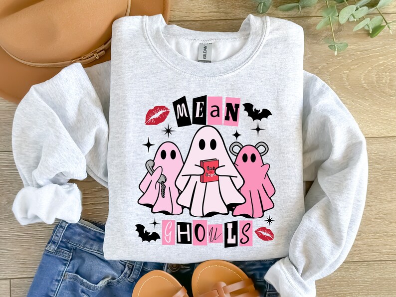 Pu&ograve; includere: Una felpa grigia con un design grafico rosa e nero con tre fantasmi e il testo "Mean Ghouls".