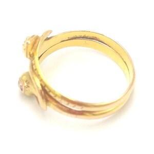 May include: A gold-toned ring with two small, round gemstones. The ring has a unique, intertwined design, with a smooth, polished finish. The gemstones are set in decorative settings, adding a touch of elegance. The ring is likely made of gold or a gold-colored metal.