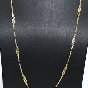 Könnte beinhalten: Eine lange goldene Halskette mit einer Reihe von gleichmäßig verteilten, länglichen, durchbrochenen Filigrangliedern. Die Kette besteht aus feinen, dünnen Kettengliedern, die jedes dekorative, symmetrische, rautenförmige Metallelement verbinden.