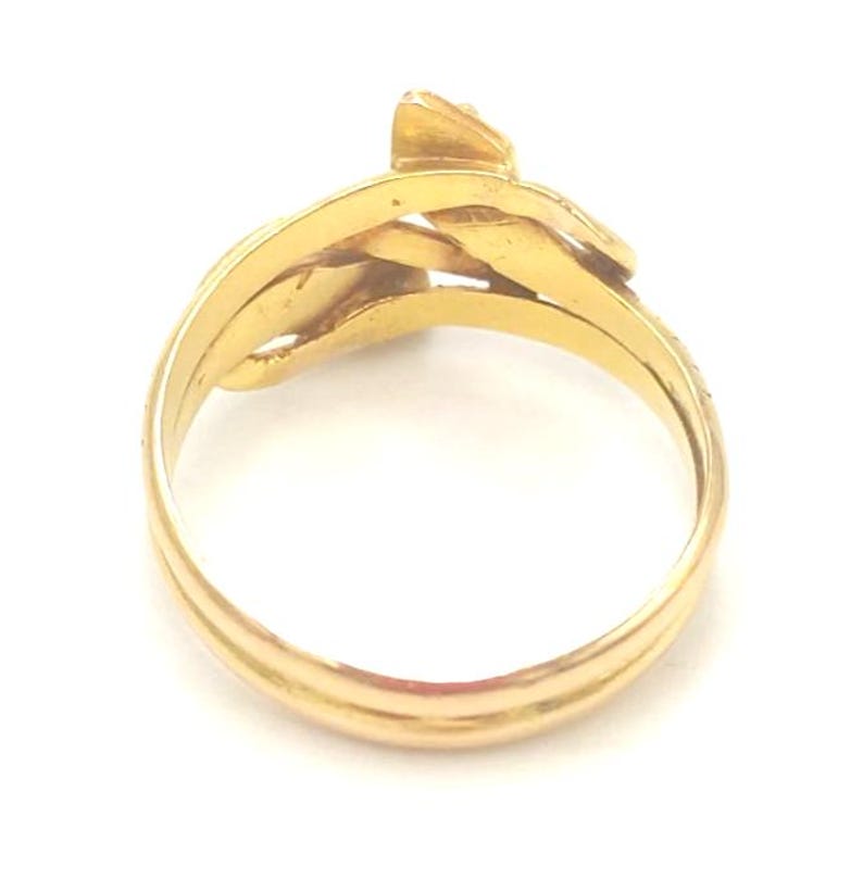 May include: A gold-colored ring with a unique, interwoven design. The ring features a series of curved bands and a small, raised element at the top. The ring's surface has a polished, reflective finish, and it sits against a white background.