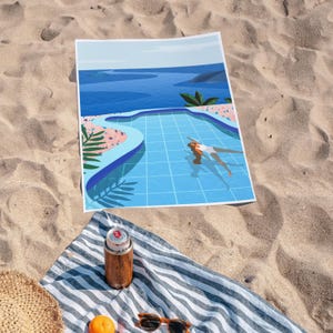 May include: A beach scene print showing a blue pool and a person swimming, with a blue ocean in the background. The print is on a white rectangular towel with blue and white stripes. A wooden can cooler, sunglasses, and a straw hat are also visible.