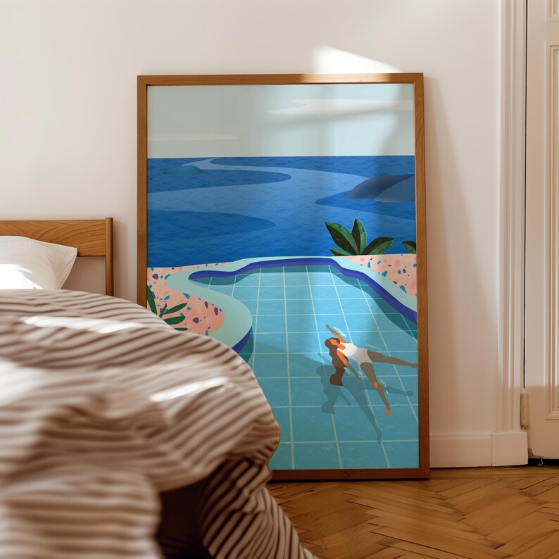 May include: A framed art print showing a person in a turquoise pool, with a blue ocean and sky. The artwork has a minimalist style, with a wooden frame. A bed with striped bedding is in the foreground.