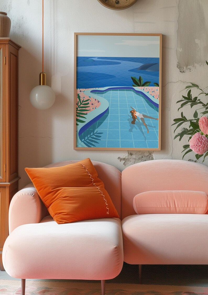 May include: A framed art print shows a person swimming in a blue pool, with a view of the sea. An orange velvet cushion rests on a pink sofa. A round, white globe light hangs from the ceiling.