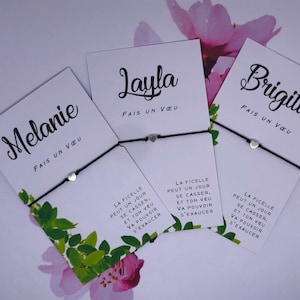 Peut inclure: Trois cartes blanches avec du texte noir et des bracelets en ficelle noire avec des breloques en forme de cœur argenté. Les cartes portent les noms "Melanie", "Layla" et "Brigitte" écrits en cursive. Chaque carte porte le texte "FAIS UN VEU" écrit sous le nom. Le texte sur les cartes est le suivant : "LA FICELLE PEUT UN JOUR SE CASSER, ET TON VEU VA POUVOIR S'EXAUCER."