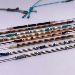 Peut inclure: Une collection de bracelets en perles avec des perles de différentes couleurs et des accents métalliques. Les bracelets sont disposés en rangée sur une surface blanche.