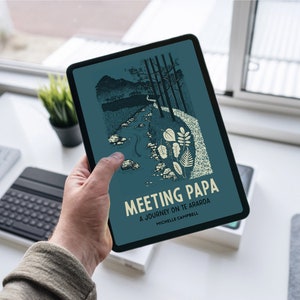 May include: A teal blue tablet displaying the cover of a book titled "Meeting Papa: A Journey on Te Araroa" by Michelle Campbell. The cover features a black and white illustration of a path through a forest with a stream running alongside it.