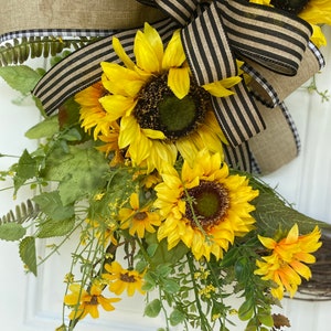 Close up of lower portion of wreath showing  sunflowers and greenery nestled into the bow.