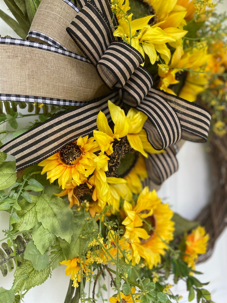 Side view of wreath showing placement of sunflowers blossoms and bow made from coordinating ribbon of burlap and black.