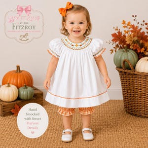 May include: A white short-sleeved dress with hand-smocked embroidery featuring orange and green floral patterns at the neckline and sleeves. The dress is paired with orange and white gingham bloomers and an orange hair bow accessory.