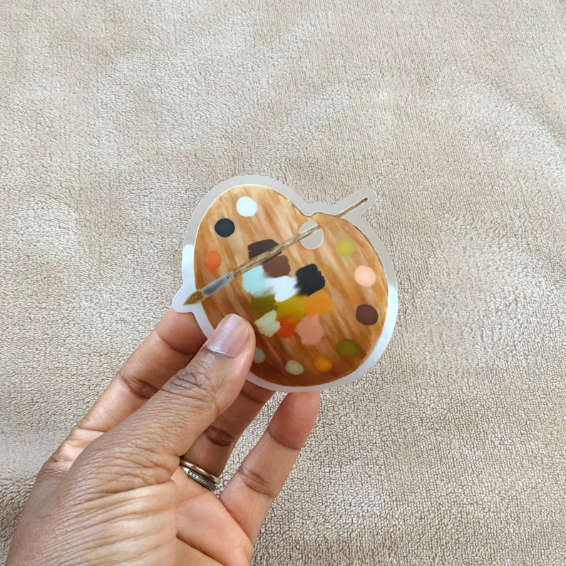 May include: A clear plastic sticker of a wooden artist's palette with a paintbrush and various coloured paint swatches.
