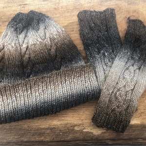 May include: A brown, gray, and white knit hat and matching fingerless gloves. The hat has a cable knit pattern and the gloves have a cable knit pattern.