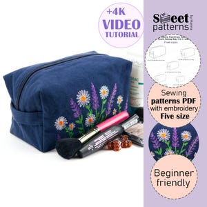 May include: A navy blue makeup bag with a floral embroidery design of white daisies and purple lavender. The bag has a zipper closure and a handle. The image also includes makeup brushes and the text "+4K VIDEO TUTORIAL".