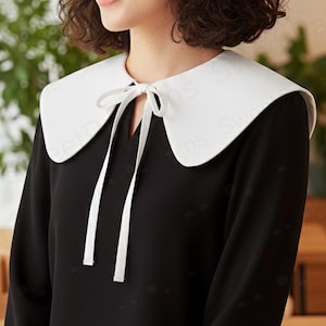 May include: A black dress with a large white Peter Pan collar. The collar is tied at the neckline with a white ribbon. The dress has long sleeves and a simple, elegant design, suitable for various occasions.