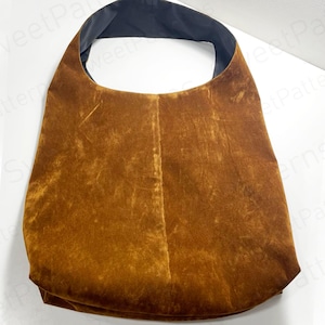 May include: A large, brown shoulder bag with a wide strap and a black interior lining. The bag has a textured, suede-like appearance and a simple, minimalist design. The bag is made of a soft material.