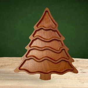 May include: A wooden Christmas tree-shaped serving tray with four indented sections. The tray is made of light brown wood and has a natural finish.