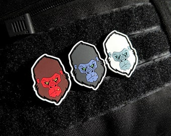 Può includere: Tre toppe ricamate con volti di gorilla in diversi colori. I volti di gorilla sono rosso, nero e bianco. Le toppe sono su uno sfondo nero.
