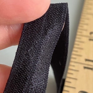 May include: Close-up of black elastic fabric with a textured weave. The fabric is folded in half and held by a finger.