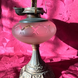 May include: A vintage oil lamp with a frosted glass shade and an ornate metal base. The shade has a geometric pattern and the base has a floral design.