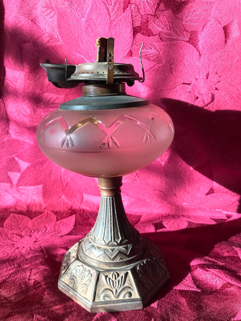 May include: A vintage oil lamp with a frosted glass shade and an ornate metal base. The shade has a geometric pattern and the base has a floral design.