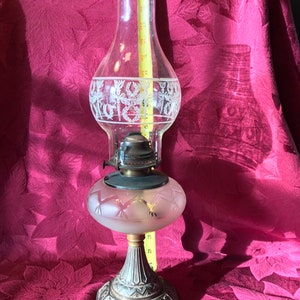 May include: A vintage glass oil lamp with a frosted glass shade and a metal base. The lamp has a decorative etched design on the glass.
