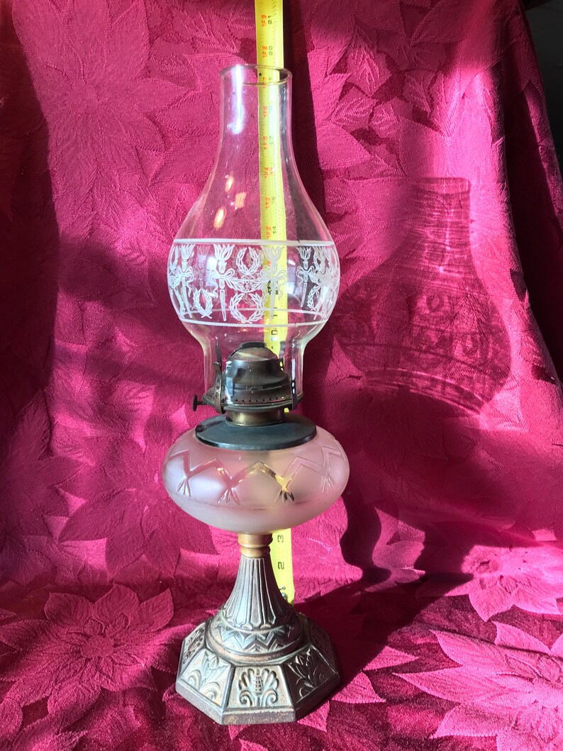 May include: A vintage glass oil lamp with a frosted glass shade and a metal base. The lamp has a decorative etched design on the glass.