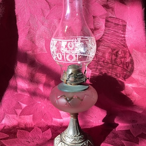 May include: A vintage oil lamp with a frosted glass shade and a silver-colored metal base. The shade has a decorative etched design of flowers and leaves.