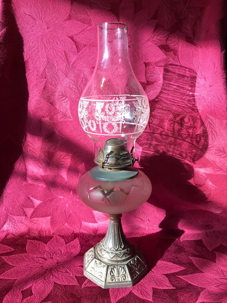May include: A vintage oil lamp with a frosted glass shade and a silver-colored metal base. The shade has a decorative etched design of flowers and leaves.