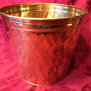 May include: A gold metal planter with a diamond pattern. The planter has a wide, round opening and a slightly tapered body.