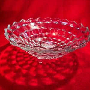 May include: A clear glass bowl with a geometric pattern and three legs. The bowl is sitting on a red surface.