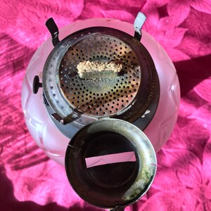 May include: A vintage glass oil lamp with a frosted white finish and a metal top. The lamp has a round shape and a decorative design. The top of the lamp has a metal wick holder and a metal cap.