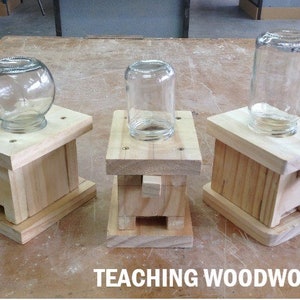 May include: Four wooden bases with glass jars on top. The bases are made of unfinished wood and have a simple design. The jars are clear glass and are different sizes and shapes. The bases are all on a wooden table. The text "TEACHING WOODWORK.COM" is visible at the bottom of the image.