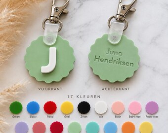 May include: Two round, scalloped-edge light green keychains with silver lobster clasps. One shows the white letter J on the front, while the other displays the engraved name Juna Hendriksen on the back. Below, 17 small colored circles show available options.