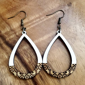 May include: A pair of wooden teardrop-shaped earrings with a white painted top and a brown geometric pattern on the bottom.