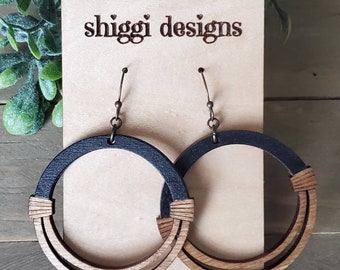 May include: A pair of wooden hoop earrings with a two-tone design. The top portion of the hoops is black, while the bottom is natural wood. The earrings are attached to a brown card with the text "shiggi designs".