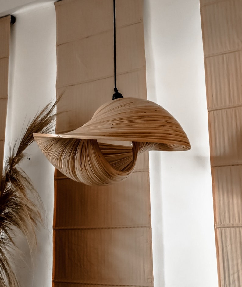 Op de afbeelding: Een unieke, handgemaakte hanglamp. De lampenkap is gemaakt van gelaagde, gebogen houten strips, waardoor een wervelend, open ontwerp ontstaat. De lamp hangt aan een zwart snoer, tegen een neutrale achtergrond.