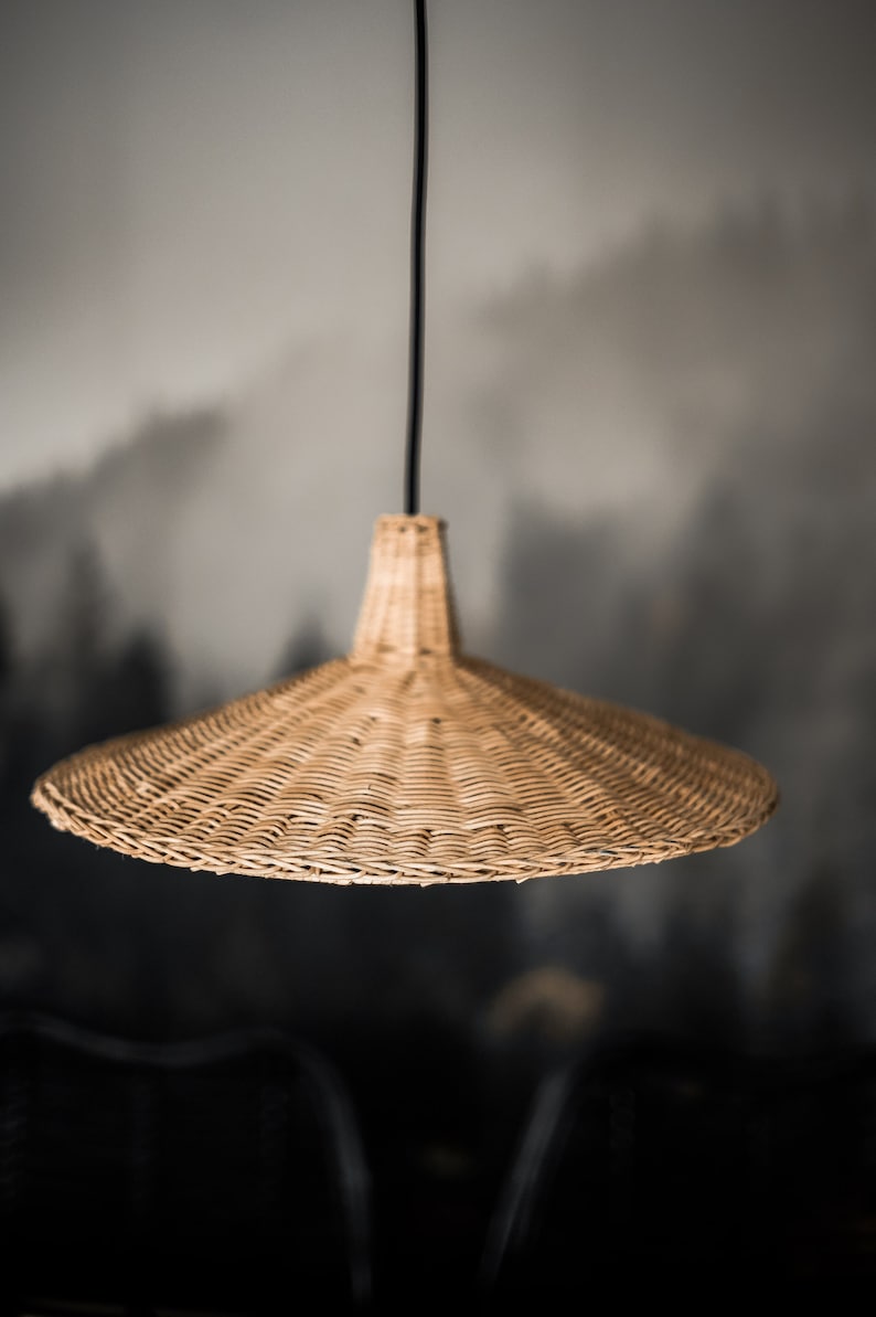 K&ouml;nnte beinhalten: Eine geflochtene H&auml;ngeleuchte aus Weide mit einem breiten, flachen, kegelf&ouml;rmigen Schirm, der an einem schwarzen Kabel h&auml;ngt.