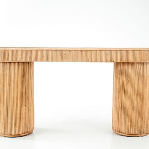 May include: A light brown, oval-shaped console table. The table features a natural, woven bamboo design. The table has two cylindrical legs and a matching top. The table is suitable for a living room or entryway.