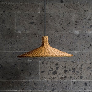 K&ouml;nnte beinhalten: Eine geflochtene H&auml;ngeleuchte aus Weide h&auml;ngt an einem schwarzen Kabel vor einer grauen Steinwand.