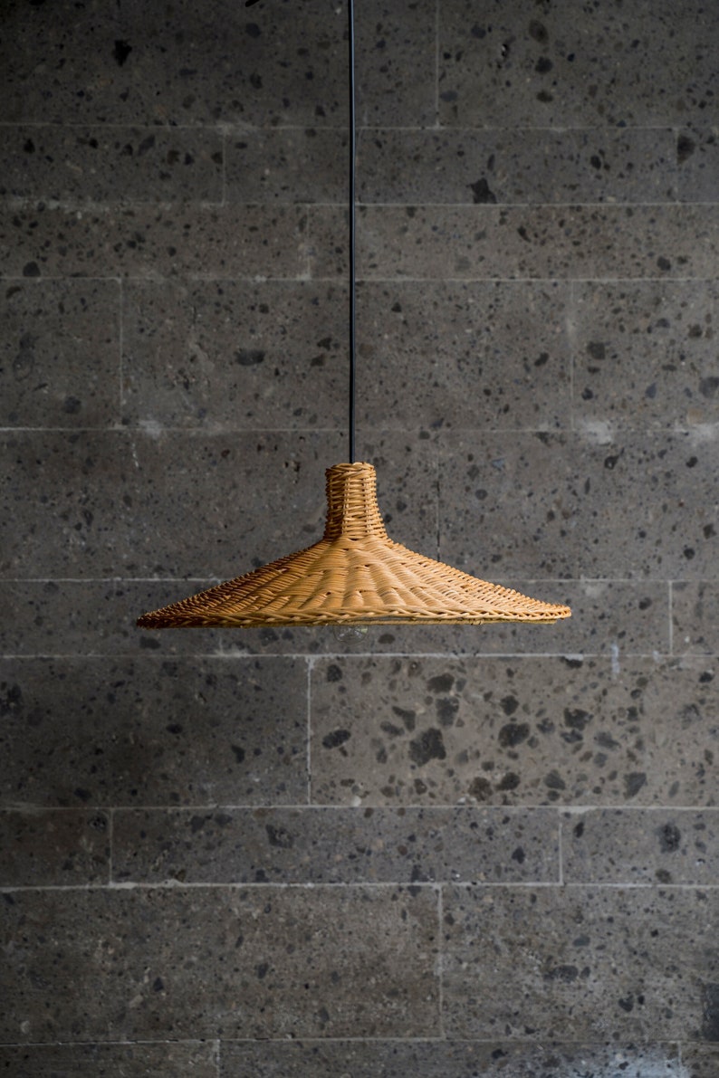 K&ouml;nnte beinhalten: Eine geflochtene H&auml;ngeleuchte aus Weide h&auml;ngt an einem schwarzen Kabel vor einer grauen Steinwand.