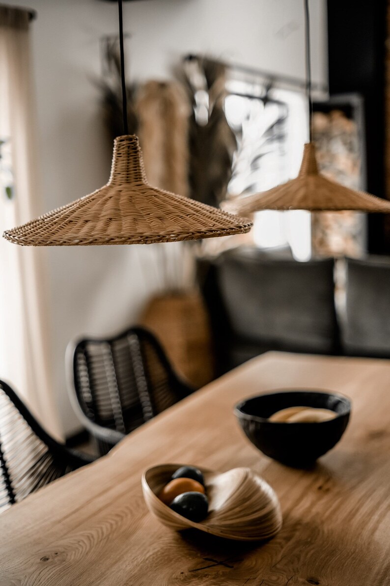 K&ouml;nnte beinhalten: Zwei geflochtene H&auml;ngeleuchten aus Weide h&auml;ngen &uuml;ber einem Holztisch mit einer Schale Obst und zwei St&uuml;hlen.