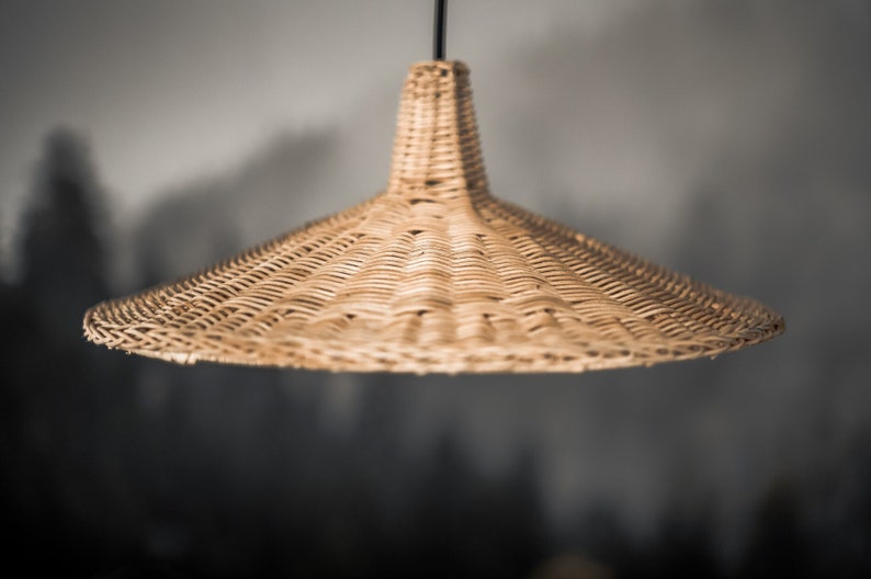 K&ouml;nnte beinhalten: Eine geflochtene H&auml;ngeleuchte aus Weide mit einem breiten, konischen Schirm. Die Leuchte h&auml;ngt an einem schwarzen Kabel.